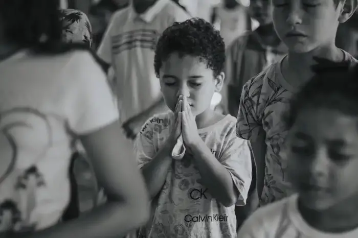 A little boy closing his eyes with his hands raised in prayer