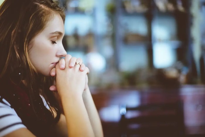 woman folding her hands in prayer with her eyes closed
