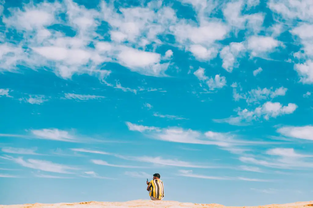 man sitting on the sand with blue sky and clouds